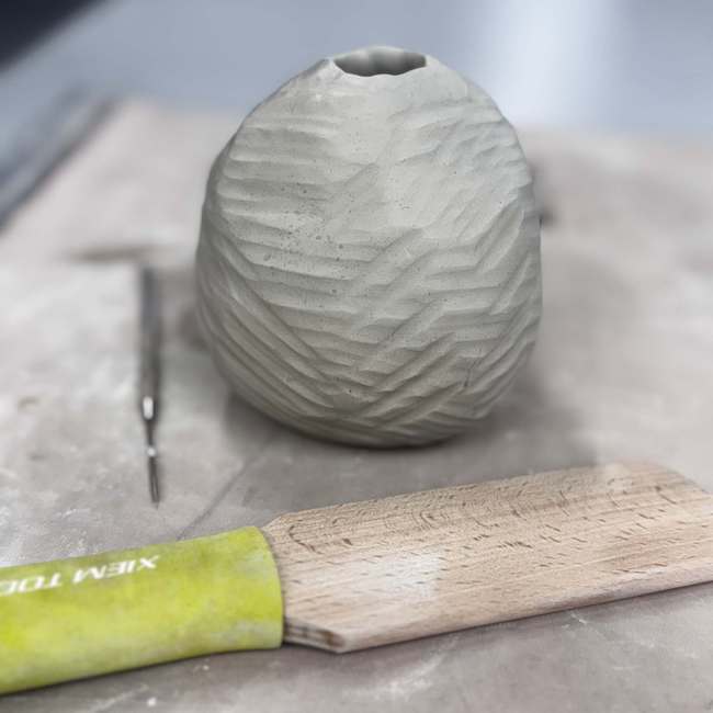 Pottery vessel in process with tool laying in front on a table.